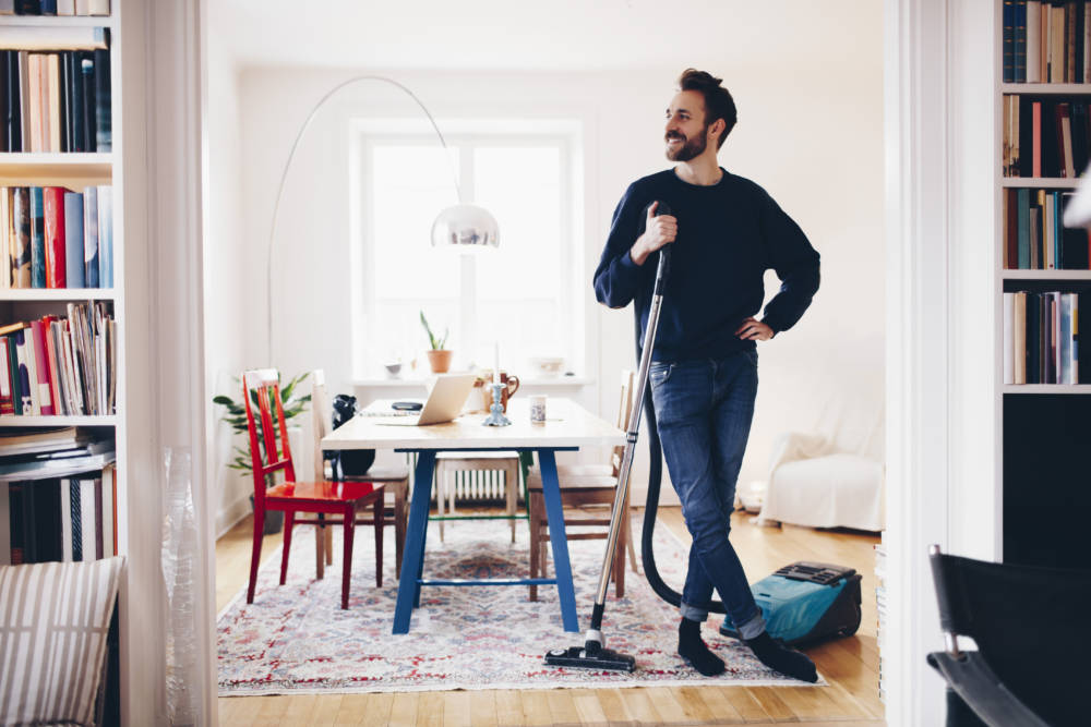 Happy man standing with vacuum cleaner in dining room at home